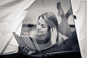 Beautiful girl lying in a tent and reading an e-book