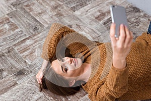 Beautiful girl lying on wooden floor and making selfie