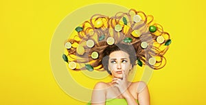 Beautiful girl lying on yellow background with citrus fruits in long hair making choice,young woman head with lemon slices and