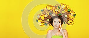 Beautiful girl lying on yellow background with citrus fruits in long hair making choice,young woman head thinking