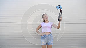 Beautiful girl makes selfie outdoors. teenager is photographed on a smartphone using small tripod. young girl blogger