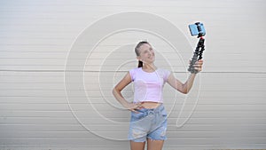 Beautiful girl makes selfie outdoors. teenager is photographed on a smartphone using small tripod. young girl blogger