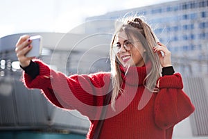 A beautiful girl makes selfie in the rays of the autumn sun. Red sweater and abstract architecure