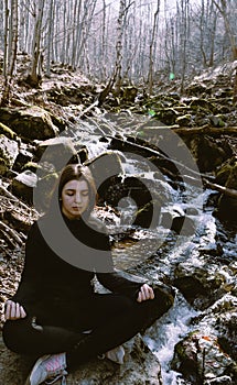 Beautiful girl making Yoga Pose lotus Sitting in a rock on a river Meditating in the forest with sunlight