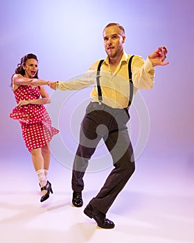Beautiful girl and man in colorful retro style costumes dancing incendiary dances isolated on lilac color background in