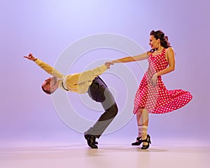 Beautiful girl and man in colorful retro style costumes dancing incendiary dances  on lilac color background in