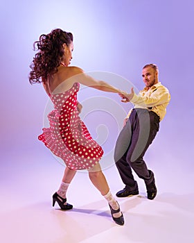 Beautiful girl and man in colorful retro style costumes dancing incendiary dances  on lilac color background in