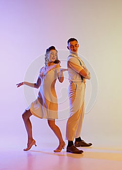 Beautiful girl and man in retro style costumes dancing incendiary dances isolated on gradient lilac color background in