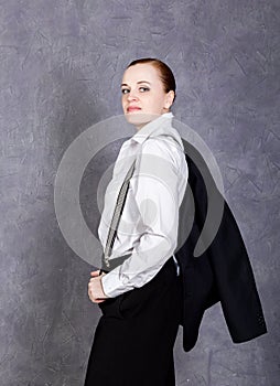 Beautiful girl in man`s suit, white shirt and suspenders poses on a gray background