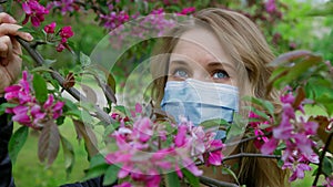 Beautiful girl in a mask sniffs cherry flowers