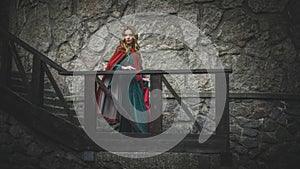 Beautiful girl in the medieval green dress with cape on the stairs