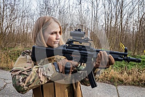 Beautiful girl in military uniform with an airsoft gun standing on the road