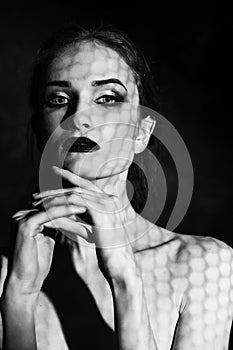 Beautiful girl model with red lips make up and naked shoulders covered with a shadow mask in the form of a net of hexagonal