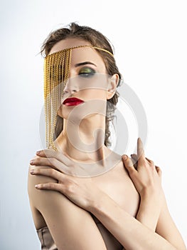Beautiful girl model with red lips make-up and naked shoulders wearing a conceptual fashion jewelry made of gold chains on her