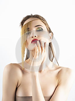 Beautiful girl model with red lips make-up and naked shoulders wearing a conceptual fashion jewelry made of gold chains on her