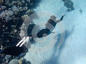 Beautiful girl with monofin swims near coral reef