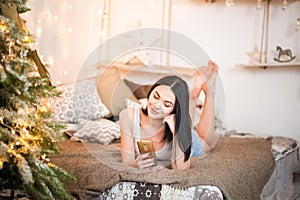 Beautiful girl in the morning with a cup in the New Year`s interior. Woman at home at Christmas time in a bedroom in a rustic styl