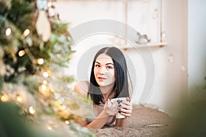 Beautiful girl in the morning with a cup in the New Year`s interior. Woman at home at Christmas time in a bedroom in a rustic styl