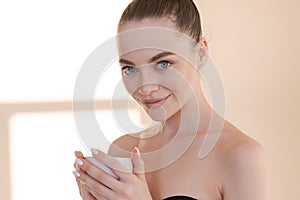 Beautiful girl with mug in her hand stands against background wall with rays