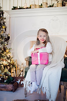 Beautiful girl near Christmas tree unpacking presents sitting on a chair