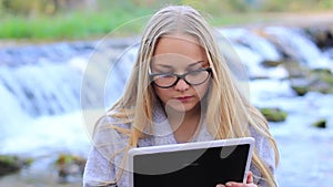 Beautiful girl near the waterfall with a tablet