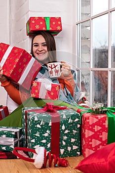 A beautiful girl in an orange jacket opens a New Year`s gift in a box with tape. Christmas Day, New Year`s Eve