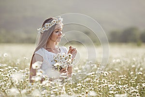 Beautiful woman in a wreath of real flowers, with a bouquet in a field of white daisies