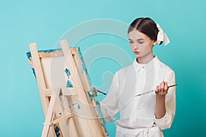 beautiful girl painting on easel with brush and palette