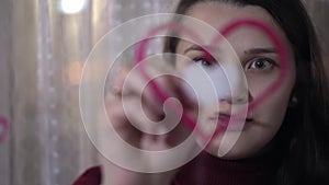 Beautiful girl paints a heart on glass