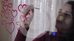 Beautiful girl paints a heart on glass
