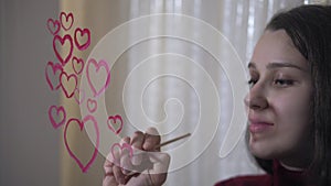 Beautiful girl paints a heart on glass