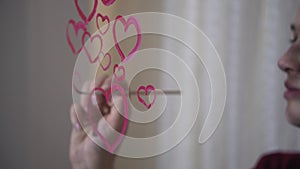 Beautiful girl paints a heart on glass