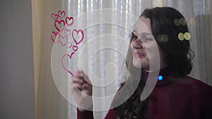 Beautiful girl paints a heart on glass