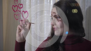 Beautiful girl paints a heart on glass