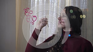 Beautiful girl paints a heart on glass