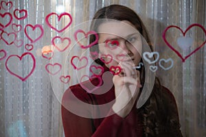 Beautiful girl paints a heart on glass