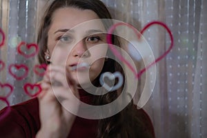 Beautiful girl paints a heart on glass