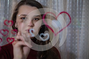 Beautiful girl paints a heart on glass