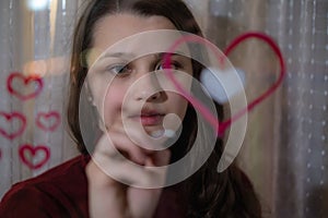 Beautiful girl paints a heart on glass