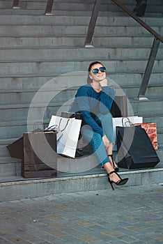 Beautiful girl with paper bags sits on a stairs outside shopping mall