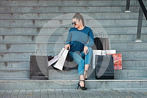 Beautiful girl with paper bags sits on a stairs outside shopping mall