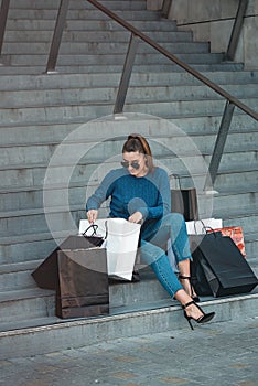 Beautiful girl with paper bags sits on a stairs outside shopping mall