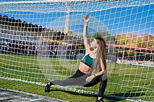 A beautiful girl with a perfect figure stands near a football goal at the stadium.  Fitness and healthy lifestyle concept