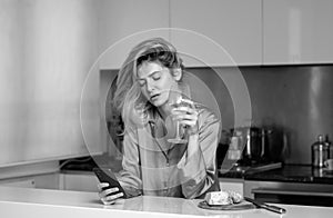 Beautiful girl with phone drinking wine in kitchen. Morning of pretty woman housewife.