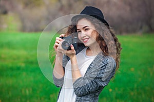 Beautiful girl-photographer with curly hair holds a camera and make a photo, spring outdoors in the park.