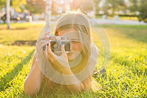 Beautiful girl photographer holds a camera and lying on the grass in the spring outdoors in the park. The concept of