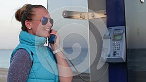 Beautiful girl picks up the phone dials the number of a payphone on the street