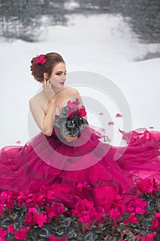 A beautiful girl in a pink ball gown with cyclamen flowers on the background of a winter forest.