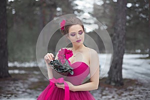 A beautiful girl in a pink ball gown with cyclamen flowers in her hands on the background of a winter forest.