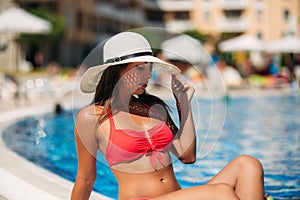 A beautiful girl in a pink bathing suit sunbathing by the pool. Sunny weather. Summer.